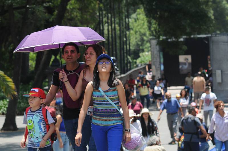 Una familia camina por Chapultepec utilizando una sombrilla para protegerse del sol.