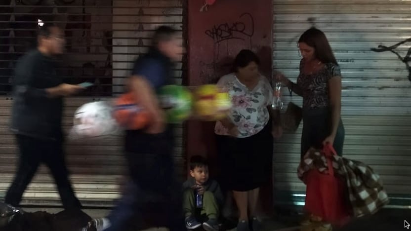 un niño espera sentado mientras la prisa del Centro pasa en ráfagas con regalos de último minuto