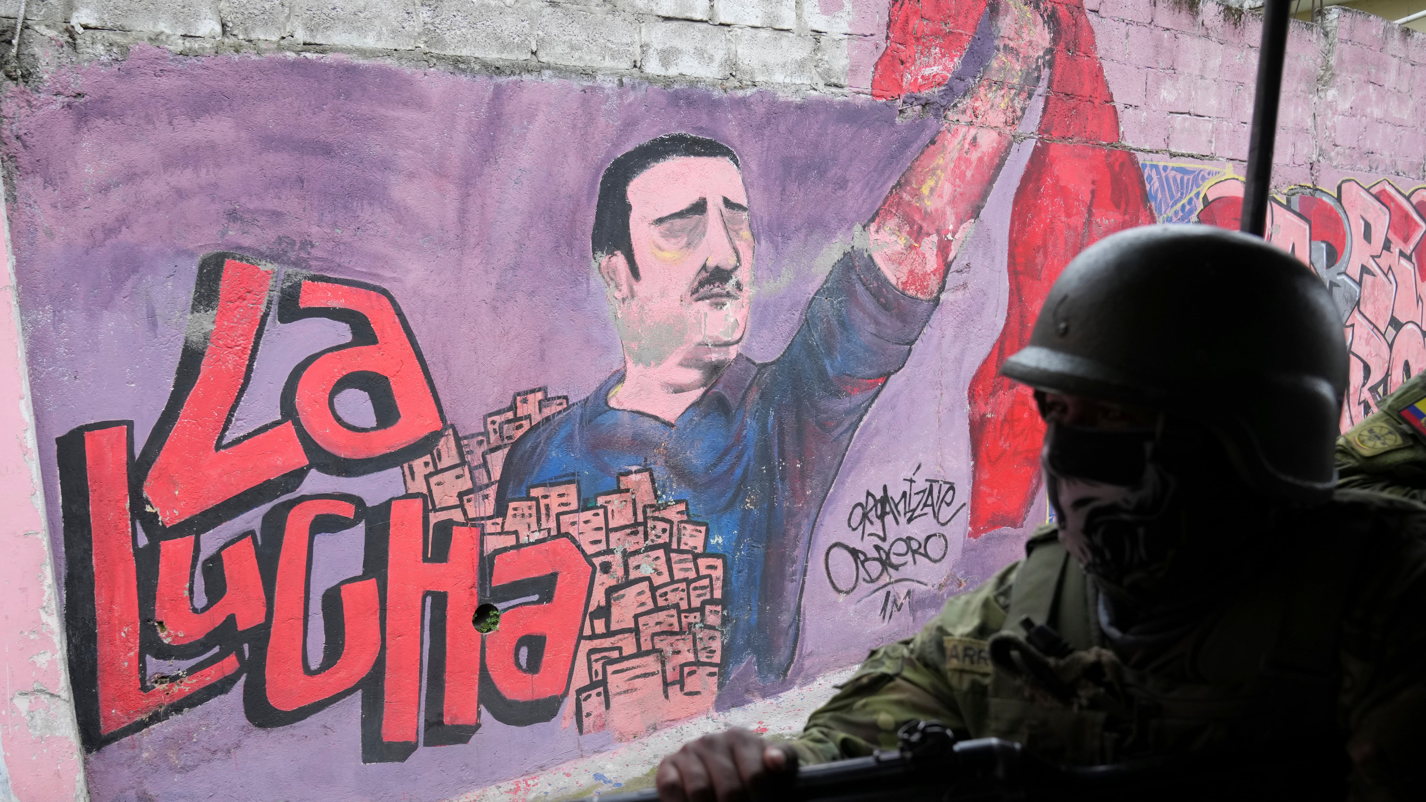 Soldados patrullan frente a un mural de un movimiento político que dice en español "La lucha" en una zona residencial en el lado sur de Quito, Ecuador, el viernes 12 de enero de 2024. A raíz de la aparente fuga de un poderoso líder de una pandilla de prisión, el presidente Daniel Noboa decretó el lunes el estado de emergencia nacional, una medida que permite a las autoridades suspender los derechos de las personas y movilizar a los militares. (Foto AP/Dolores Ochoa)