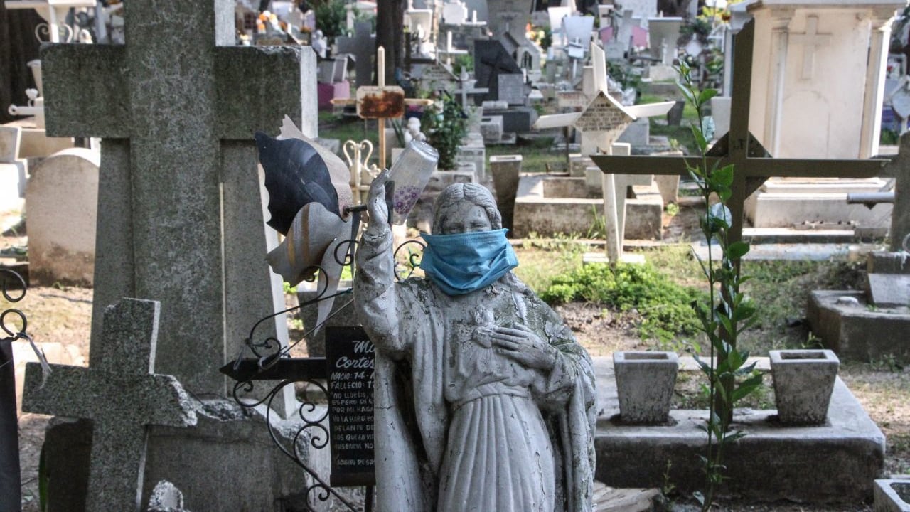 Estatua religiosa de tumba es tapada con cubrebocas en el panteón San Francisco.