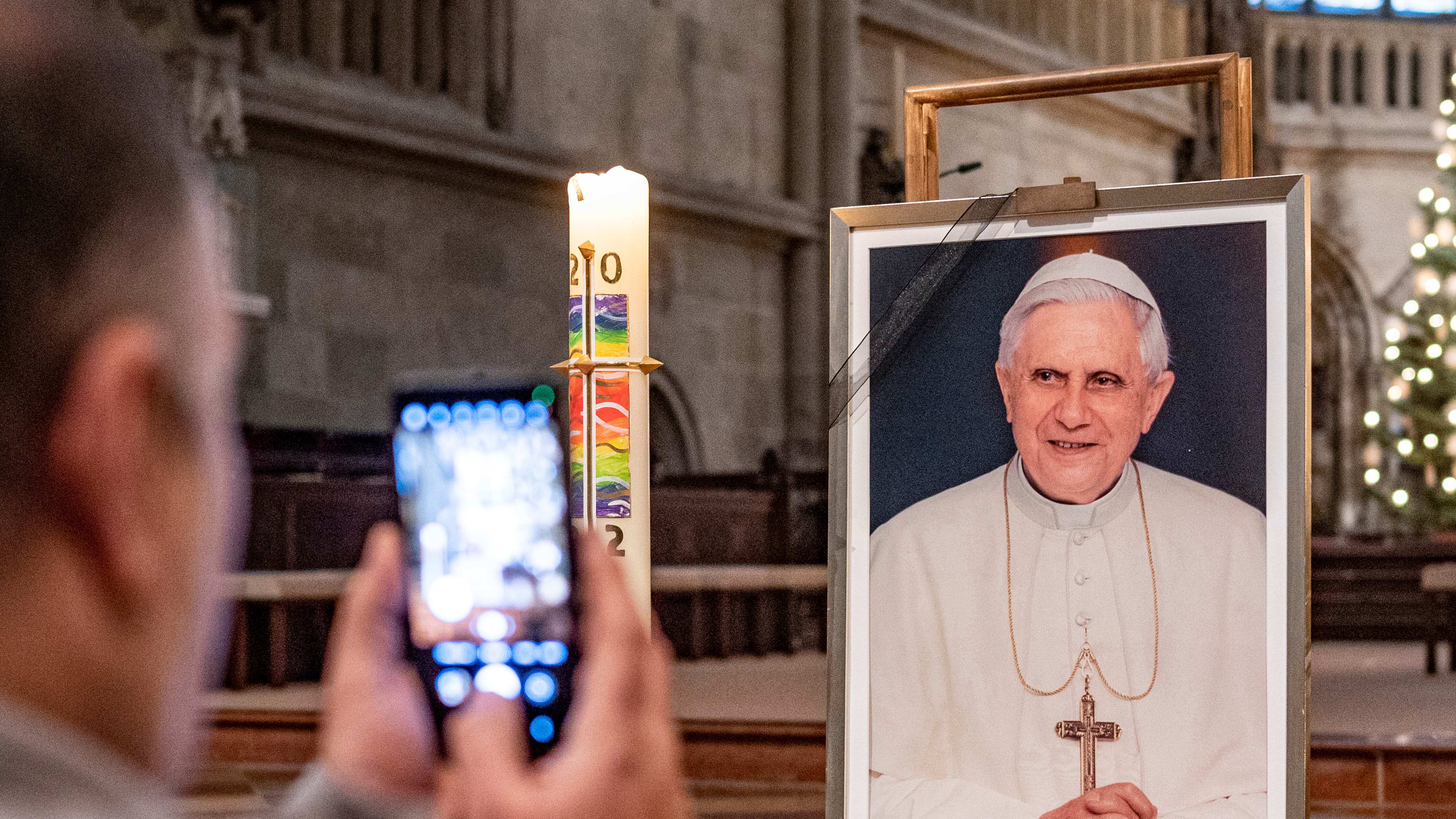 Una persona toma una foto de un retrato del Papa Emérito Benedicto XVI en la Catedral de San Pedro en Ratisbona, Alemania, el sábado 31 de diciembre de 2022. El papa emérito Benedicto XVI, el teólogo alemán que será recordado como el primer papa en 600 años en renunciar, ha muerto, anunció el Vaticano el sábado. Tenía 95 años (Armin Weigl/dpa via AP)