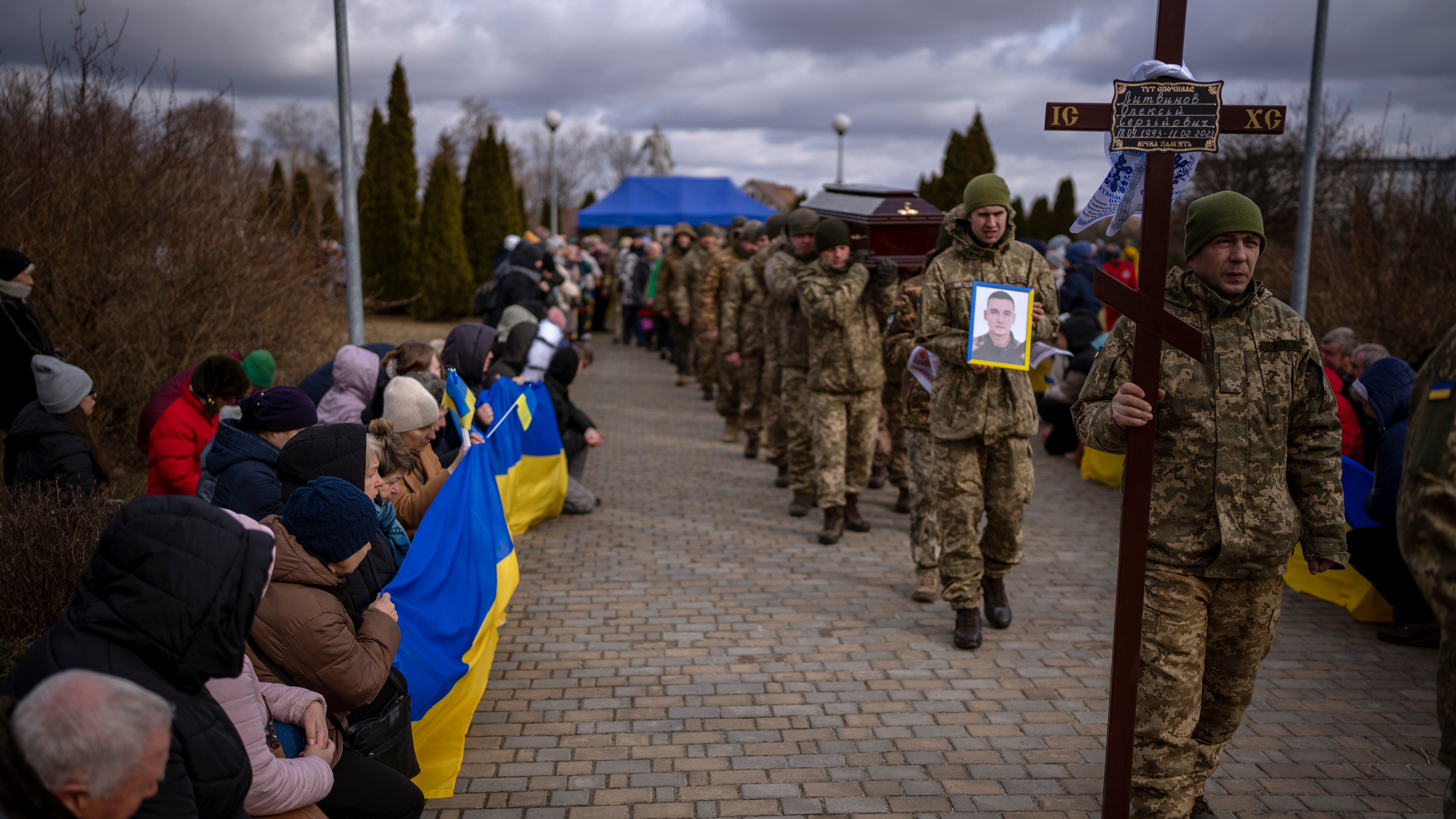 People kneel as the funeral procession with the body of Oleksii, 29, passes by during his funeral in Brovary, near Kyiv, Ukraine, Sunday, Feb. 19, 2023. Oleksii Lytvynov was a civilian who joined the Ukrainian Armed Forces to defend Kyiv when the Russian full-scale war started and was killed on Feb. 11, during battle for Vuhledar in the southeast of the country. (AP Photo/Emilio Morenatti)