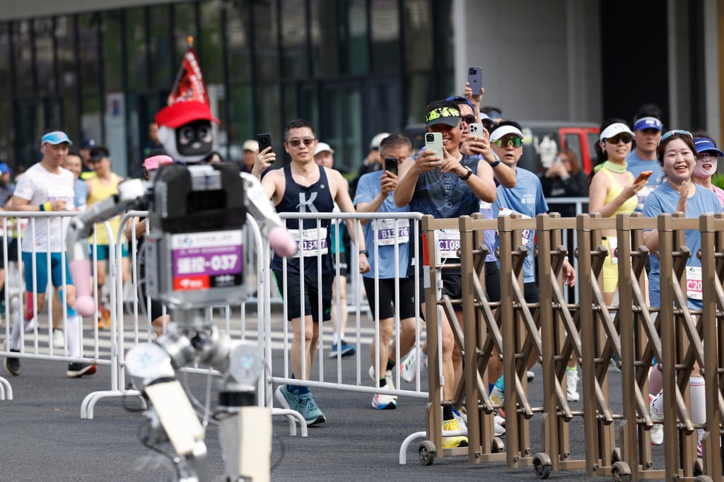 Corredores toman fotos de un robot humanoide en la II Media Maratón y Media Maratón de Robots Humaoides Beijing E-Town en Beijing. (Haruna Furuhashi/Pool Foto via AP)
