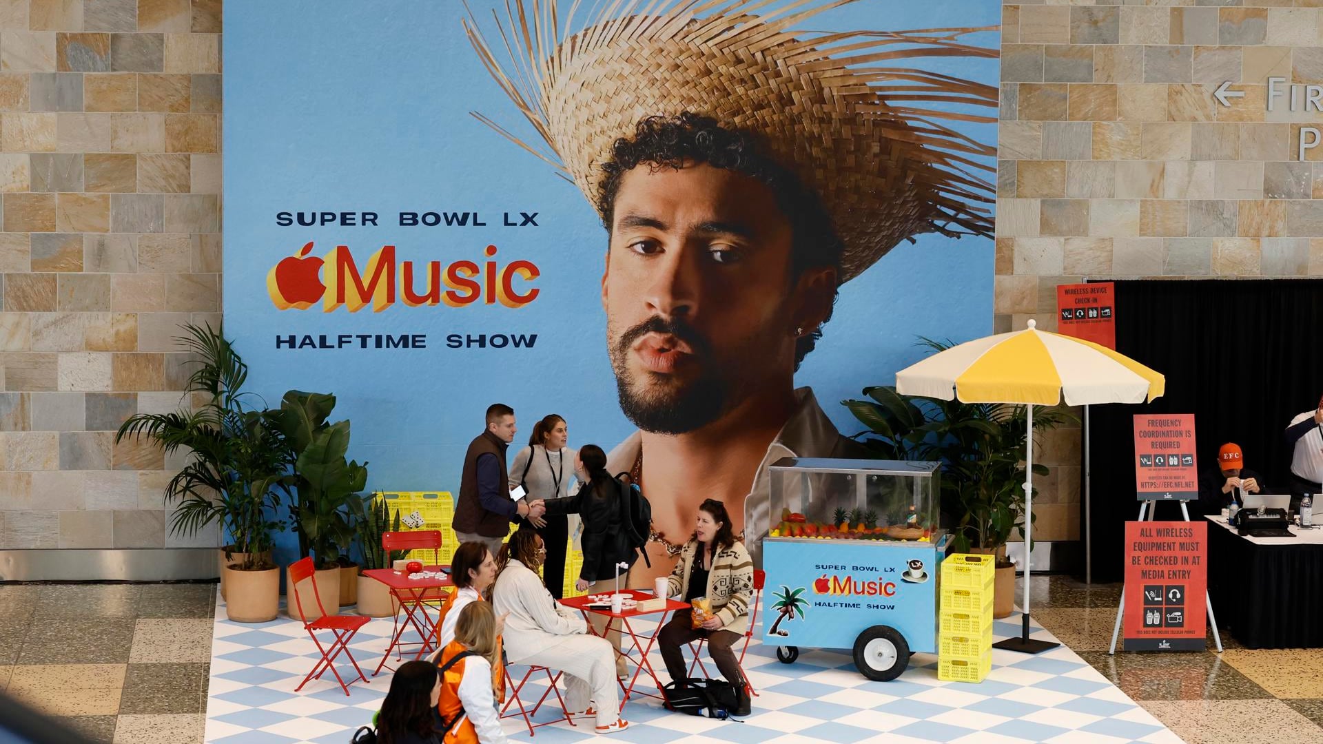 Gente sentada junto a un cartel del cantante Bad Bunny, protagonista del espectáculo del medio tiempo del Super Bowl, que se disputa este domingo. EFE/EPA/JOHN G. MABANGLO