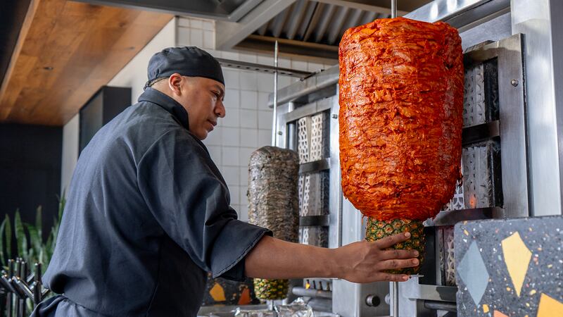 Taquero preparando el trompo de pastor rojo tradicional.