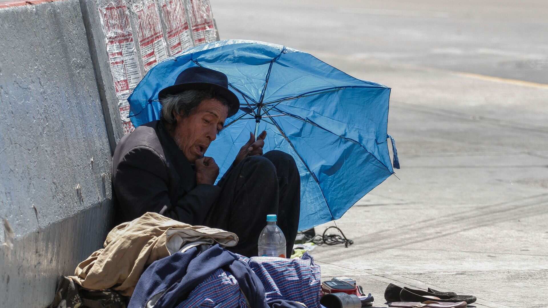Un indigente se cubre del sol y el calor con un viejo paraguas.