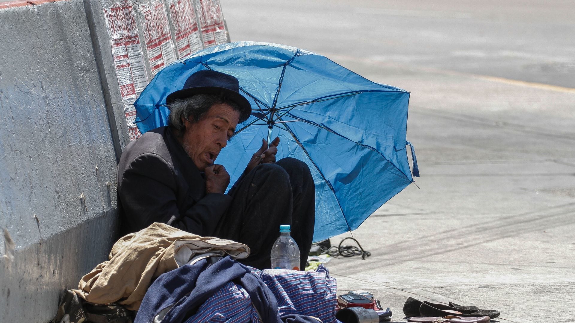 Un indigente se cubre del sol y el calor con un viejo paraguas.