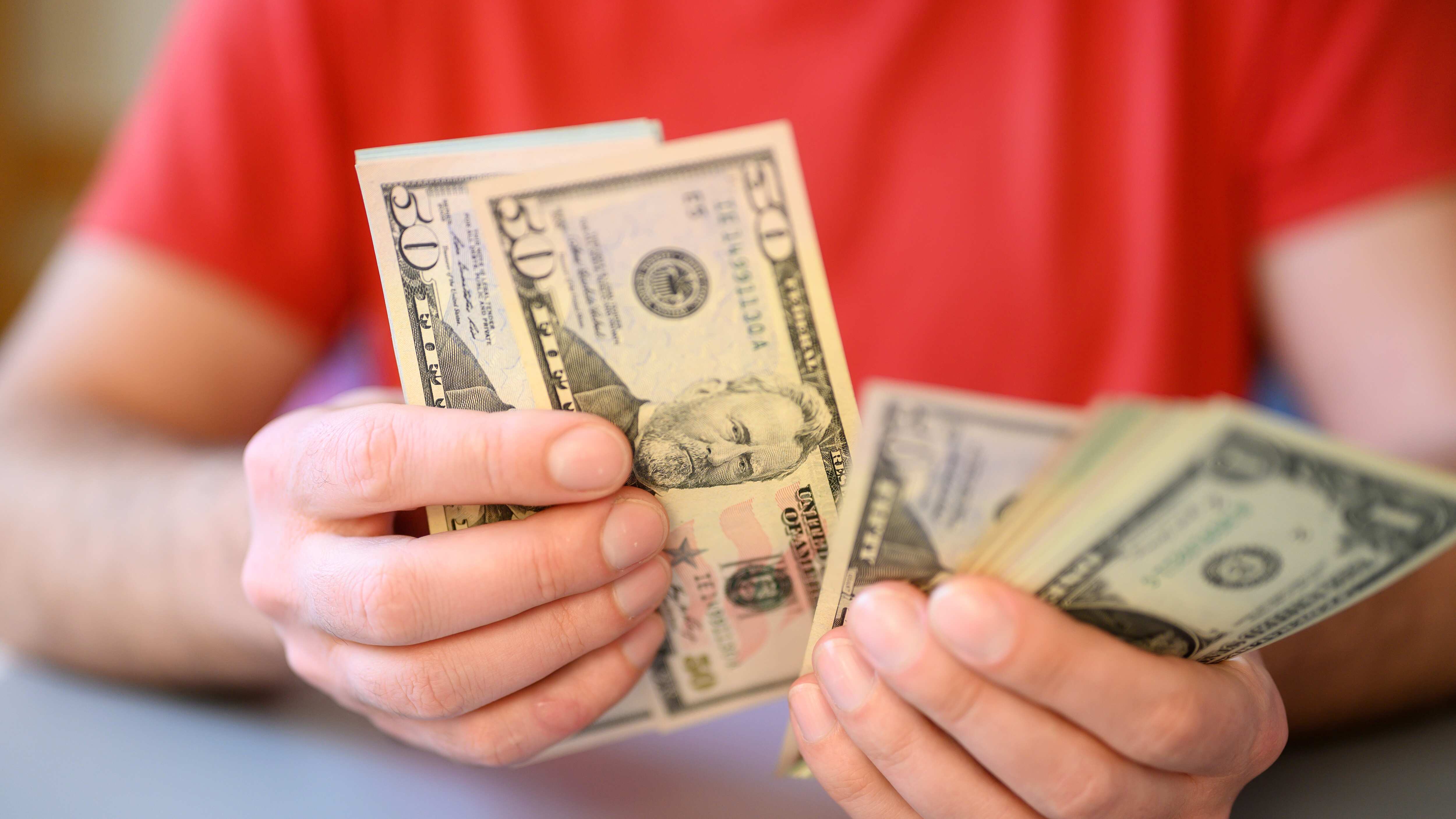 Las manos de los hombres sostienen y cuentan billetes de 50 y 1 dólar en una mesa gris