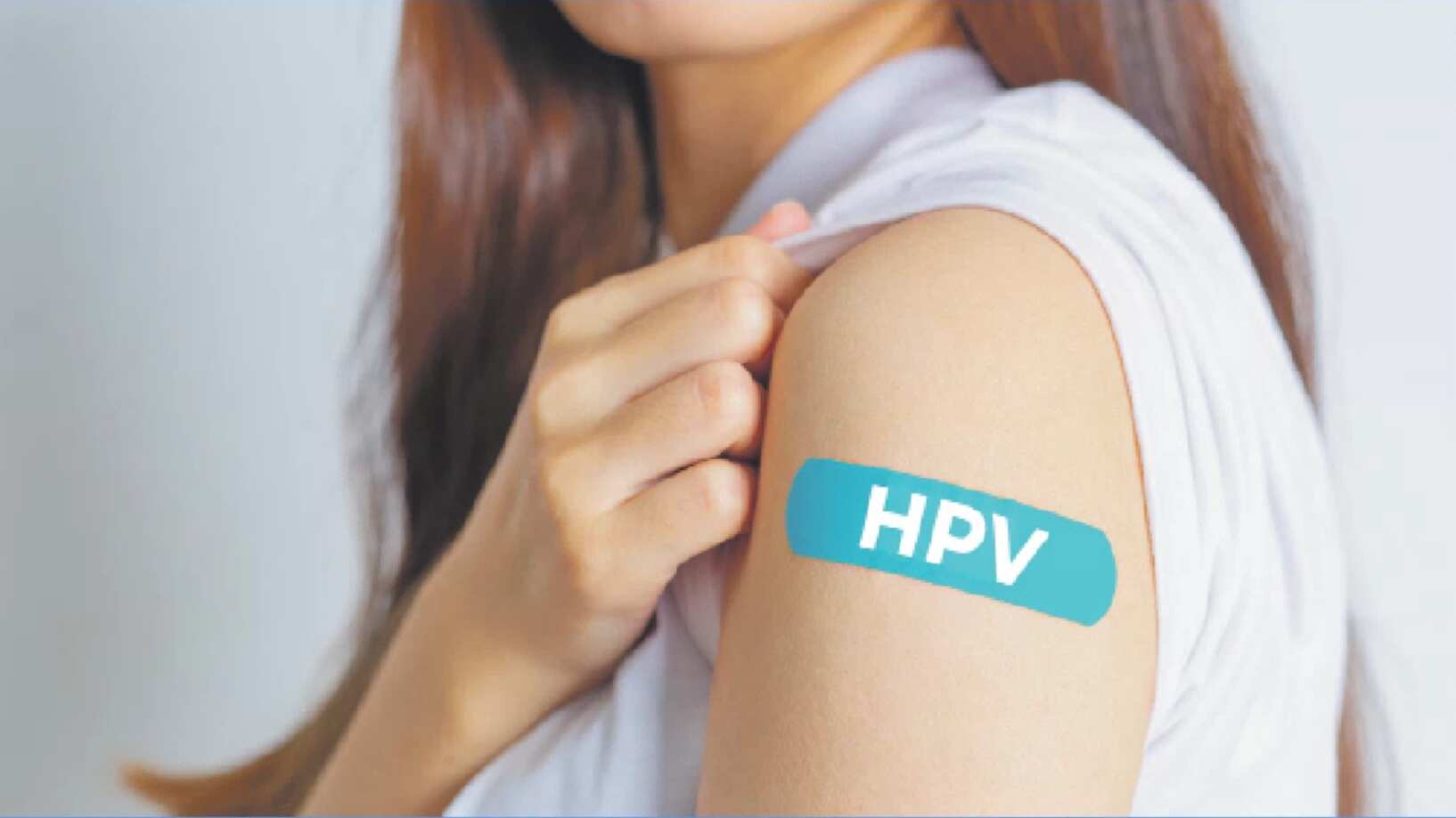 Una mujer muestra su brazo con una curita color "teal", o verde azulado, que lee "HPV" haciendo referencia a la vacuna contra el virus del papiloma humano.