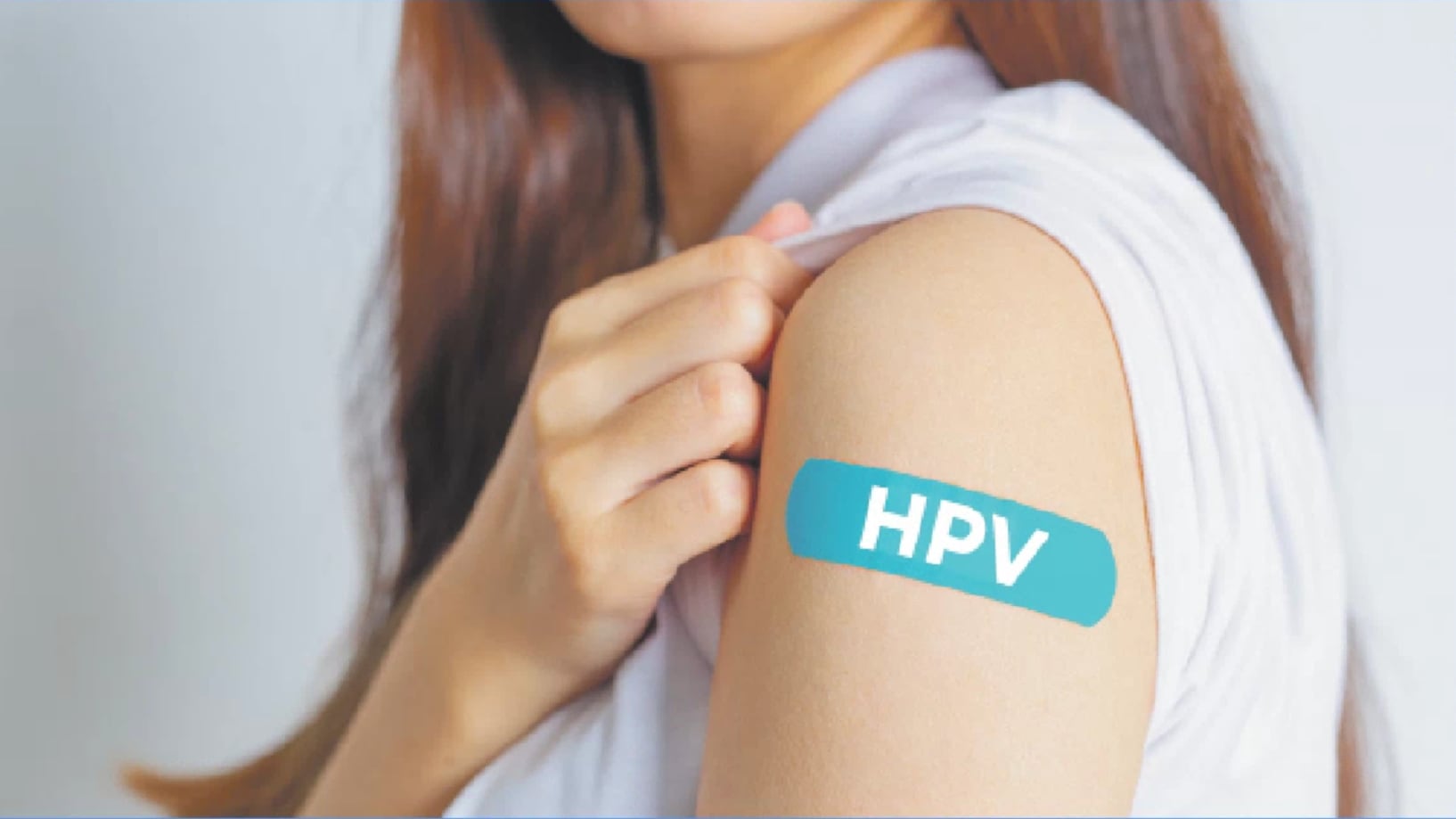 Una mujer muestra su brazo con una curita color "teal", o verde azulado, que lee "HPV" haciendo referencia a la vacuna contra el virus del papiloma humano.
