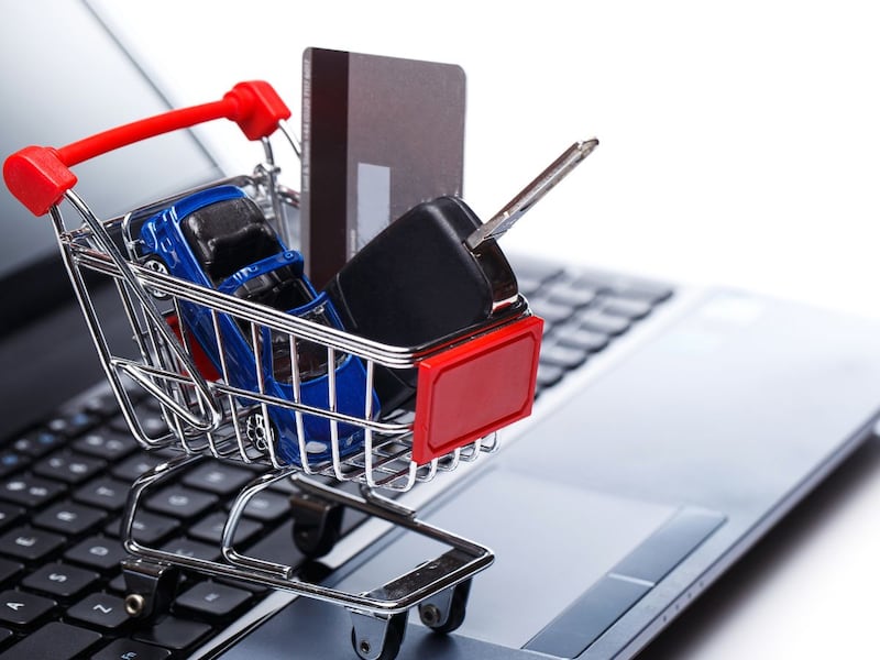 Carrito de compra con llaves de auto y tarjeta sobre una laptop, representando la compra de auto en línea